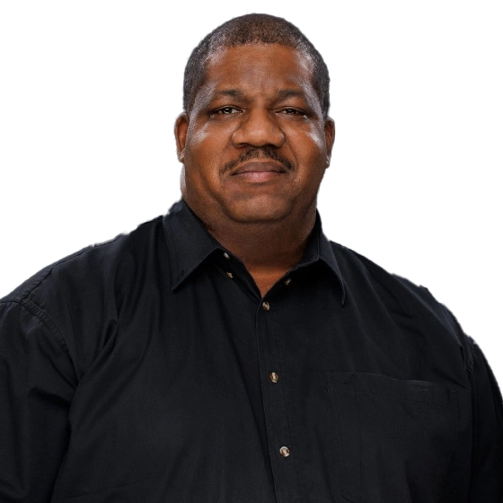 A middle-aged man with short hair and a mustache, wearing a black button-up shirt, stands in front of a dark gradient background, looking directly at the camera with a neutral expression.