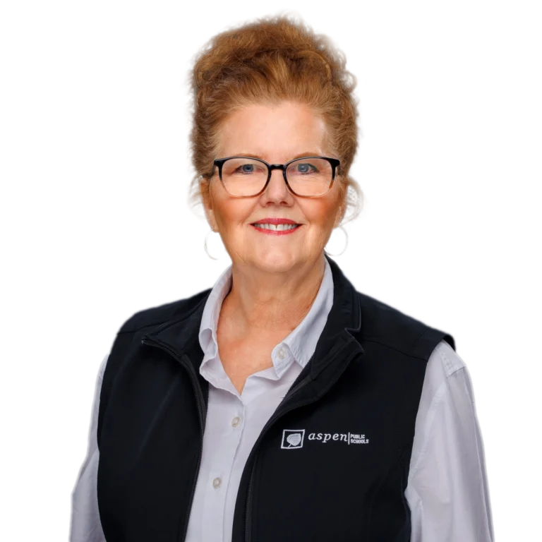 A smiling woman with glasses and red hair wears a white shirt and a black Aspen vest, standing against a white background.